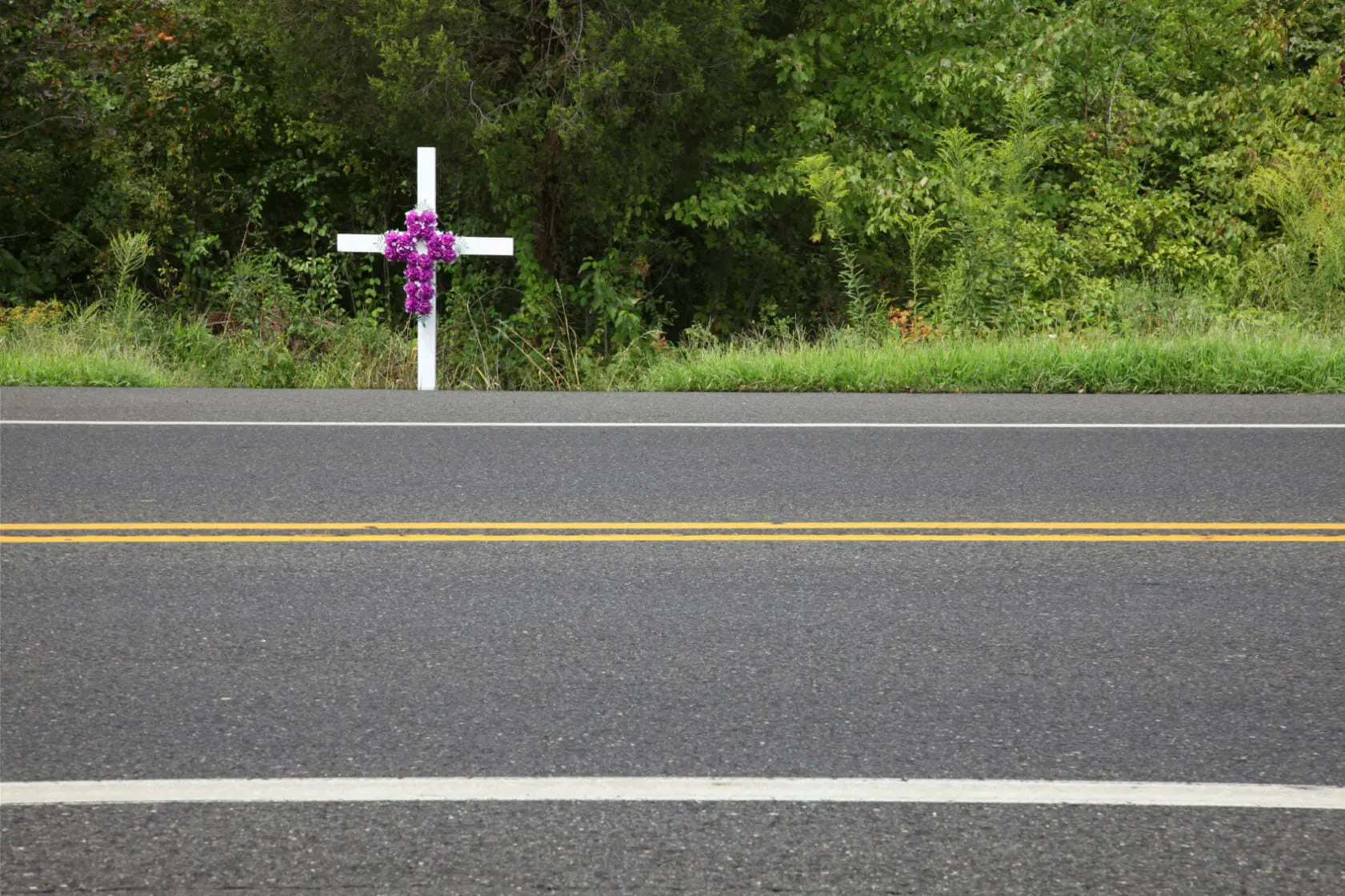Woman Killed, Husband Hospitalized in Houston Car Collision 1 A white cross with roses on it alongside a road