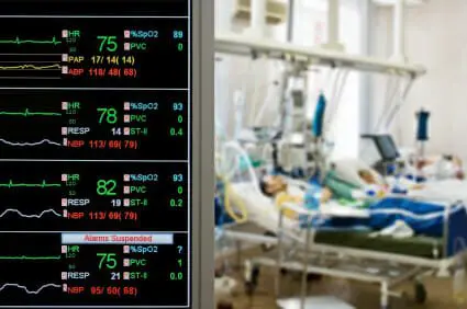 Patients in hospital bed with vital sign monitor in foreground.