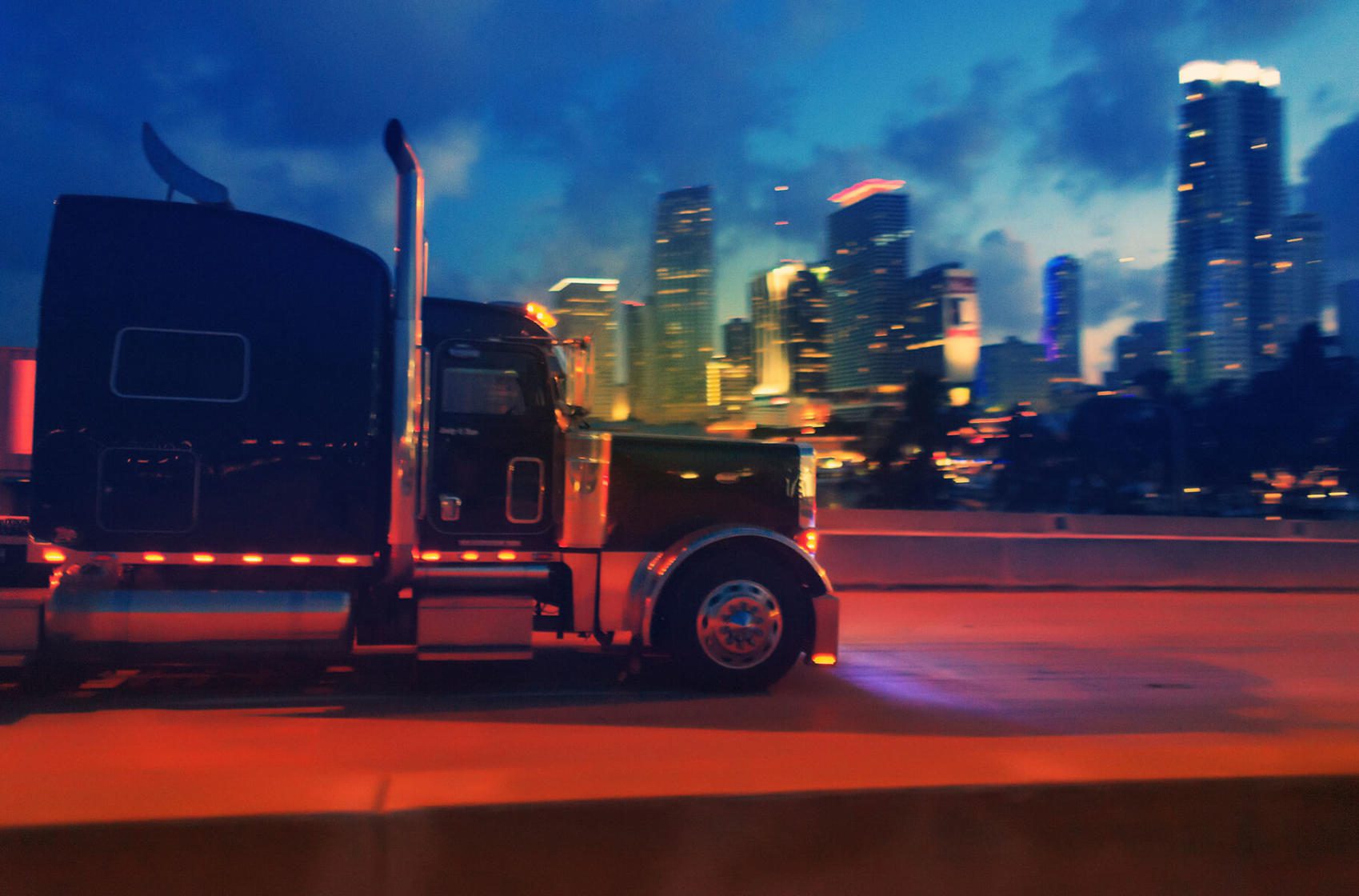 18-wheeler traveling on highway with city in background