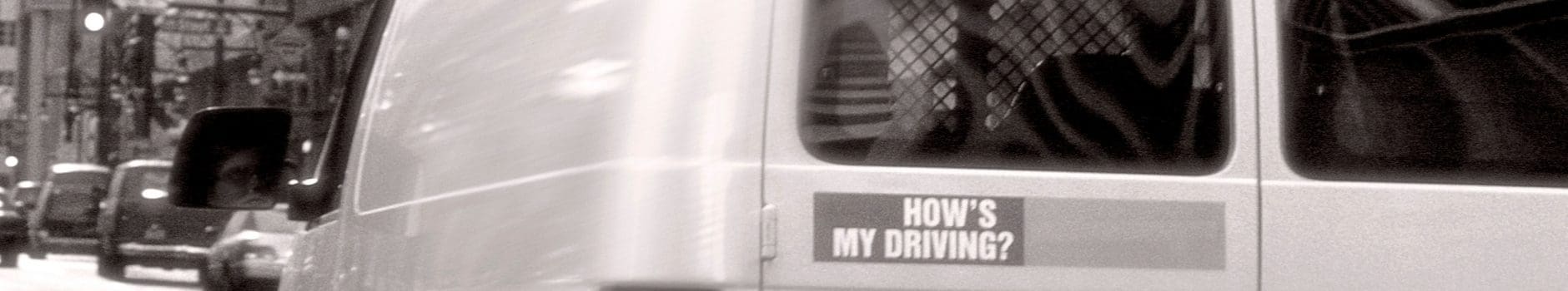 Black and white photo of back of a van with "How's my Driving?" sticker