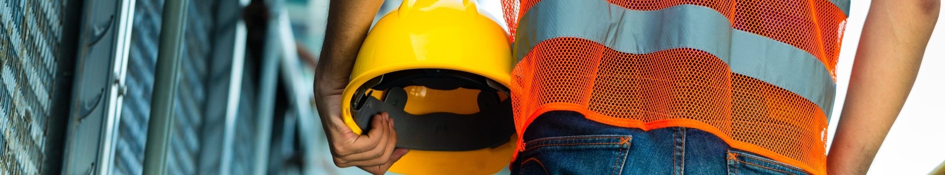 Construction worker with orange reflective safety vest holding yellow helmet